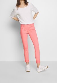 Růžové skinny džíny z bavlny s ohrnutými lemy, doplněné bílým tričkem s krátkým rukávem. Celý outfit doplňují bílé sportovní tenisky.