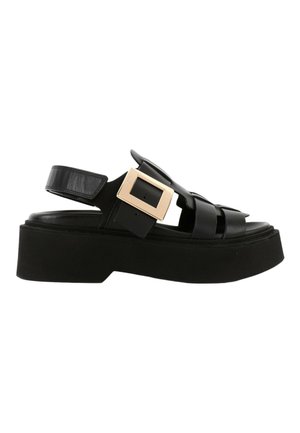 Sandale à plateforme noire avec larges brides en cuir et une grande boucle carrée dorée sur le côté.