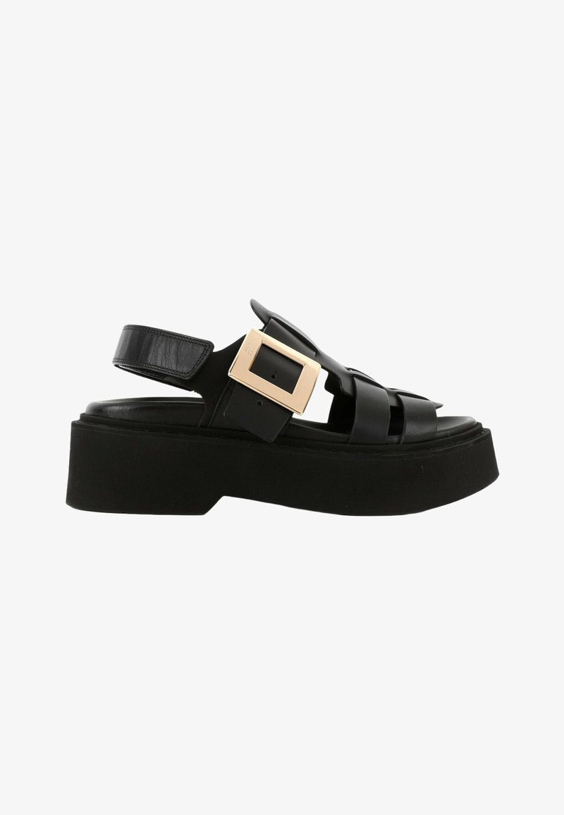 Sandale à plateforme noire avec larges brides en cuir et une grande boucle carrée dorée sur le côté.