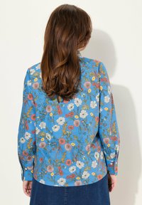 Camisa de manga larga en tela azul, con un colorido patrón floral. Textura suave, puños abotonados y detalle de dobladillo redondeado.