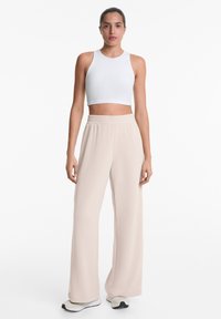 Weißes, geripptes Croptop kombiniert mit lockeren, beigen, hoch taillierten Hosen. Das Material wirkt weich mit einer glatten Textur. Minimalistisches Design.