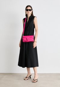 Black sleeveless dress with a collar, cinched waist; bright pink crossbody bag with a curved flap and silver hardware; black heeled sandals.
