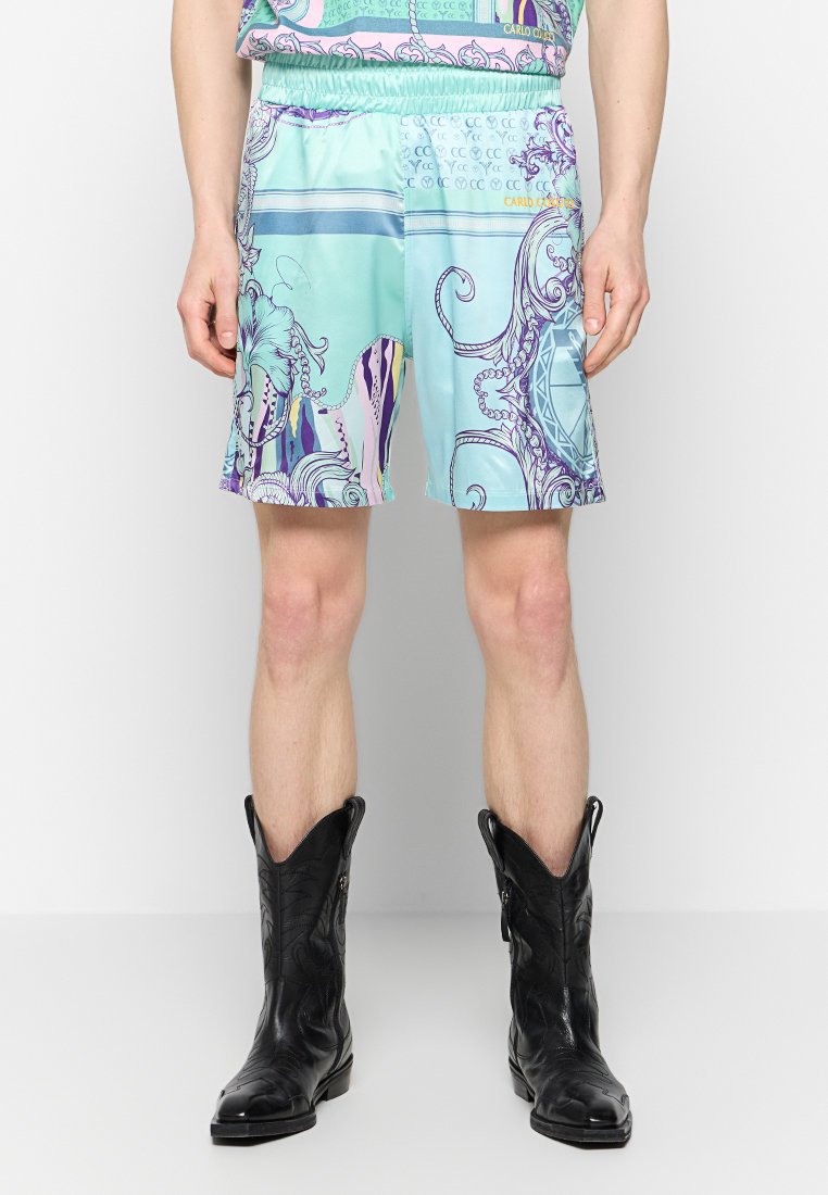 Hellblaue Shorts mit bunten abstrakten Mustern und einem elastischen Bund, kombiniert mit schwarzen Cowboy-Stiefeln aus strukturiertem Leder.