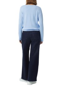 Helles blaues Strickoberteil mit runder Halslinie, kombiniert mit dunkelblauen, weit geschnittenen Jeans mit Gesäßtaschen. Weiße Sneaker runden das Outfit ab.