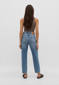 Højtaljede blå denim jeans med en løs pasform, der har to baglommer og et brunt lædermærke på taljebåndet.