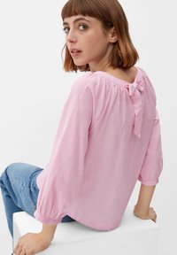 Roze gestreepte blouse met een ronde hals, 3/4 mouwen en een strikdetail op de rug. De stof lijkt lichtgewicht met een zachte textuur.