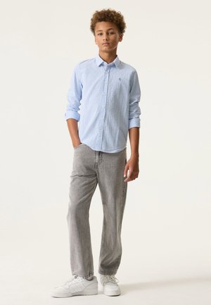 Chemise à rayures bleues et blanches à boutons, manches longues, associée à un jean gris à coupe ample et des baskets blanches. Tenue simple et décontractée.