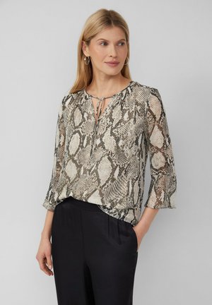 Blouse transparente avec un motif en peau de serpent dans des tons beige, noir et crème. Présente un décolleté en keyhole et des manches évasées trois-quarts.