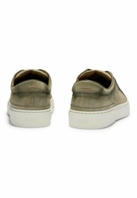 Olive green suede slip-on shoes with a white rubber sole. Features minimal stitching and a small decorative accent on the heel.