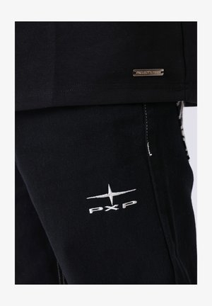Zwart katoenen overhemd met een metalen label met de tekst "PROJECT X PAND." Zwarte broek met witte "PXP" borduursel en textuurstof.
