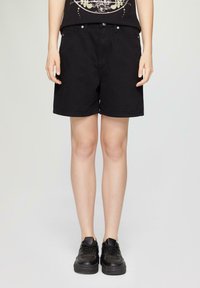 Shorts en denim noir à coupe droite, avec poches avant, passants de ceinture et fermeture à bouton. Associés à des baskets noires.