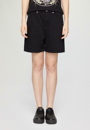 Zwarte denim shorts met een rechte snit, voorzien van voorkanten, riemlussen en een knoopsluiting. Draagt met zwarte sneakers.