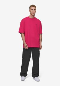 Oversized pink cotton t-shirt with short sleeves and a crew neck, paired with black cargo pants and white sneakers. Simple logo detail.