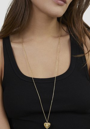 Gold chain necklace featuring a heart-shaped pendant with a star design at the center, worn over a black ribbed tank top.