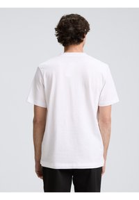 Balta trumpa rankovė t-shirt su švelniu dryžuotu tekstūru, apvaliu kaklu ir laisvu siluetu, matoma iš nugaros.