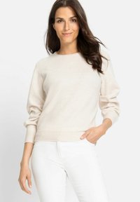 Helle beige Pullover aus weichem Stoff, mit rundem Ausschnitt, gerippten Bündchen und einem schlichten Design, kombiniert mit weißen Hosen.