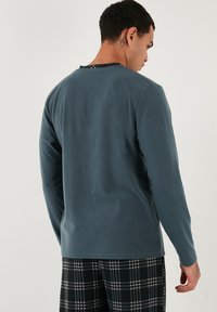 Garie pasmaku, ar apaļu kaklu, tumšas tējas krāsas krekls ar gludu faktūru un kontrastējošu raibumu detaļu pie kakla.