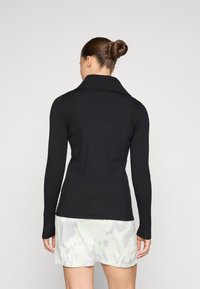 Black long-sleeve sweater with a ribbed texture, wide collar, and fitted silhouette. Worn over a light, patterned skirt.
