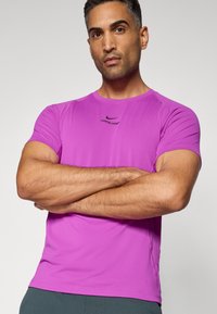 T-shirt de sport Nike Pro violet à manches courtes, au toucher doux et à la coupe ajustée. Présente un petit logo noir sur la poitrine.