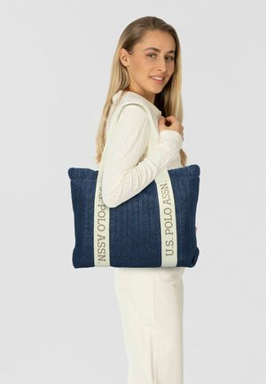 Donkerblauwe geweven draagtas met crèmekleurige banden, voorzien van de prominente opdruk "U.S. POLO ASSN.". Gestructureerd ontwerp met een getextureerde afwerking.