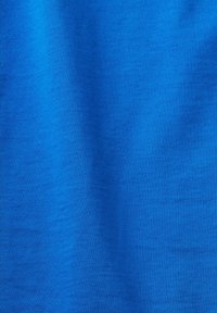 Tissu bleu avec une texture tricotée fine et lisse, présentant de subtiles plis verticaux créant de douces ombres.