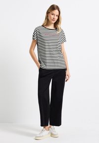 Camiseta de rayas blancas y negras con cuello redondo y mangas cortas, que presenta texto rojo. Combinada con pantalones negros holgados y zapatillas ligeras.