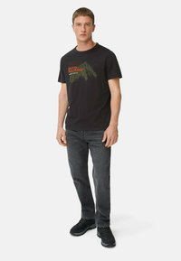 Schwarzes Grafik-T-Shirt mit Bergdruck und dem Text "Into Nature". Kombiniert mit dunklen Jeans und schwarzen Wanderschuhen.