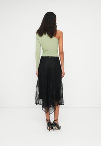 Top de mangas longas, verde claro, combinado com uma saia de renda preta, apresentando um design em camadas e uma bainha assimétrica. Sapatos de salto pretos completam o visual.