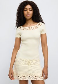 Φόρεμα με ριμπ ύφανση και κοντά μανίκια σε ανοιχτό κρεμ χρώμα, με κροσέ δαντέλα στο πάνω μέρος και στο κάτω μέρος, με κορδόνι στη μέση και υφή στη βάση.