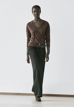 Brun V-hals sweater lagdelt over en grå langærmet skjorte, kombineret med sorte bukser med vide ben og brune ankelstøvler. Enkel, moderne påklædning.