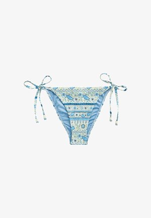 Nahaufnahme eines gemusterten blauen und weißen Bikinihöschen mit floralen Designs und gebundenen Schnüren auf gebräunter Haut.