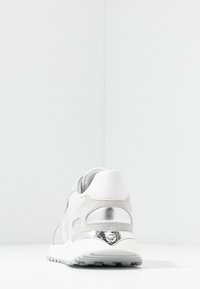 Bílé sportovní boty se stříbrnými akcenty, texturovanou síťovinou a hladkou koženkou, zaoblený tvar a silná gumová podrážka.