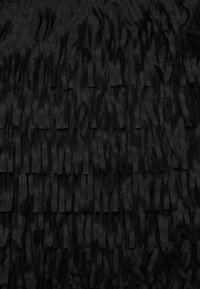 Nahaufnahme von geschichteten, schwarzen Wildlederfransen, die ein strukturiertes, dichtes und überlappendes Stoffmuster erzeugen.