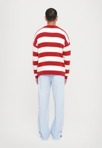 Rot-weißer gestreifter Pullover mit lockerer Passform, kombiniert mit hellblauen Nadelstreifenhosen. Der Pullover hat eine weiche Textur und weite Ärmel.