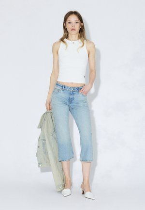 Witte nauwsluitende tanktop, lichtblauwe cropped jeans en een lichtgroene spijkerjasje. Witte mules. Simpel, schoon ontwerp met minimale details.