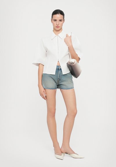Hvit kortermet bluse med glidelås foran, parret med lyseblå denimshorts med frynsete kanter, og beige spissede leppestiftsko.