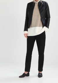 Czarna skórzana kurtka z teksturowanymi panelami, beżowy sweter z golfem, kremowy sweter, czarne eleganckie spodnie i czarne buty wsuwane.