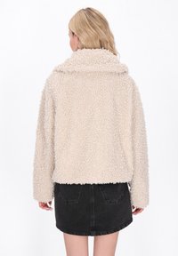 Giacca in pile beige e morbida con un ampio colletto e maniche lunghe. Il design è accorciato con un'esterno testurizzato e un orlo dritto.