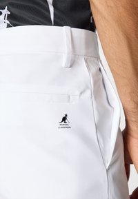 Hvite bukser laget av glatt stoff, med sidelommer og en logo på baksiden. Designet inkluderer en skreddersydd passform med en strømlinjeformet silhuett.
