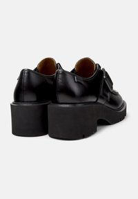 Black leather shoes with a rounded toe, low cut design, and chunky black rubber platform sole. Features a subtle brand label on the back.