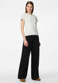 Balts ribots T-krekls ar īsām piedurknēm, kombinēts ar augstām melnām platām biksēm un brūniem čības tipa apaviem. Vienkāršs dizains, gluda tekstūra.