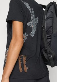 Czarny t-shirt z białą i pomarańczową mapą konturową na plecach oraz listą miejsc po bokach. Lekki materiał, krótkie rękawy.