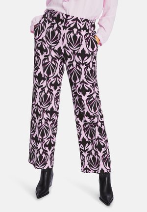 Röhrenhose in Pink mit schwarzem Blumenmuster, ausgestattet mit Seitentaschen und einem lockeren Schnitt. Getragen mit schwarzen Stiefeletten.
