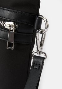 Borsa in tessuto nero con una superficie liscia, dotata di metalleria in argento, una cerniera e una tracolla rimovibile con dettagli in pelle.