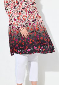 Abito floreale con design gradiente dal crema al nero, decorato con motivi di cuori colorati e pennellate. Abbinato a pantaloni capri bianchi.
