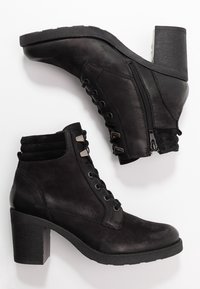 Botas de tobillo negras hechas de cuero suave con suela de goma texturizada, que presentan cordones en la parte frontal y cierre de cremallera en el lateral. Detalles de tacón bloque.