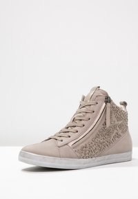 Högstövelsnike i ljusgrå mocka med dekorativa nitar på sidan, dragkedjedetaljer och en texturerad gummisula för grepp.