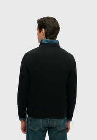 Gebreide, donkerblauwe trui met een hoge kraag, geribbelde manchetten en zoom. Draagt over een lichtblauw overhemd met denimbeslagen.