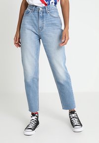 Ljust blå högmidjade jeans i denim, med raka ben, blek finish och rå fåll, tillsammans med svarta hög-top sneakers.