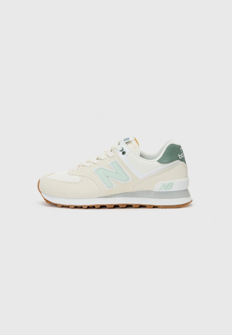 Beige and white New Balance sneaker with light green "N" logo, green heel tab, white midsole, and gum rubber outsole on gray background.